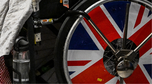 The wheel of a fencing chair with part of the GB flag showing as a spoke guard. the clamps for a fencing frame around the wheel indicate that it's being used in competition or training