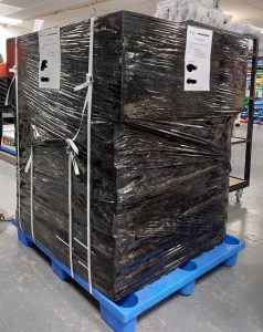 A large stack of metal frames covered in black packing wrap and standing on a pallet, having just arrived.