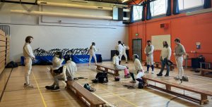A group of fencers sitting on benches in the gym practicing seated fencing activities