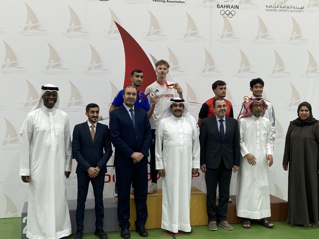 A podium photo with four fencers and several officials standing in front.