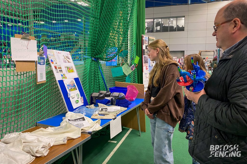 Several people are looking at an environmental sustainability stand, which features signage and old fencing equipment.