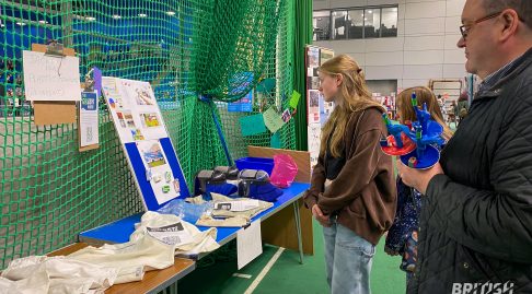 Several people are looking at an environmental sustainability stand, which features signage and old fencing equipment.