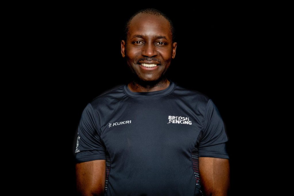 A coach in a British Fencing Kukri t-shirt smiles to the camera.