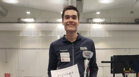A fencer smiles while holding a silver trophy and certificate.