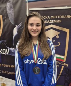 A fencer wearing a bronze medal smiles to the camera.