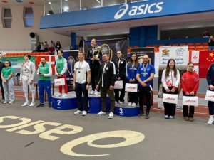 Multiple fencers stand on a podium, some with their coaches.