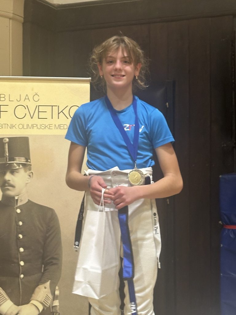 A young fencer wearing a medal smiles to the camera.