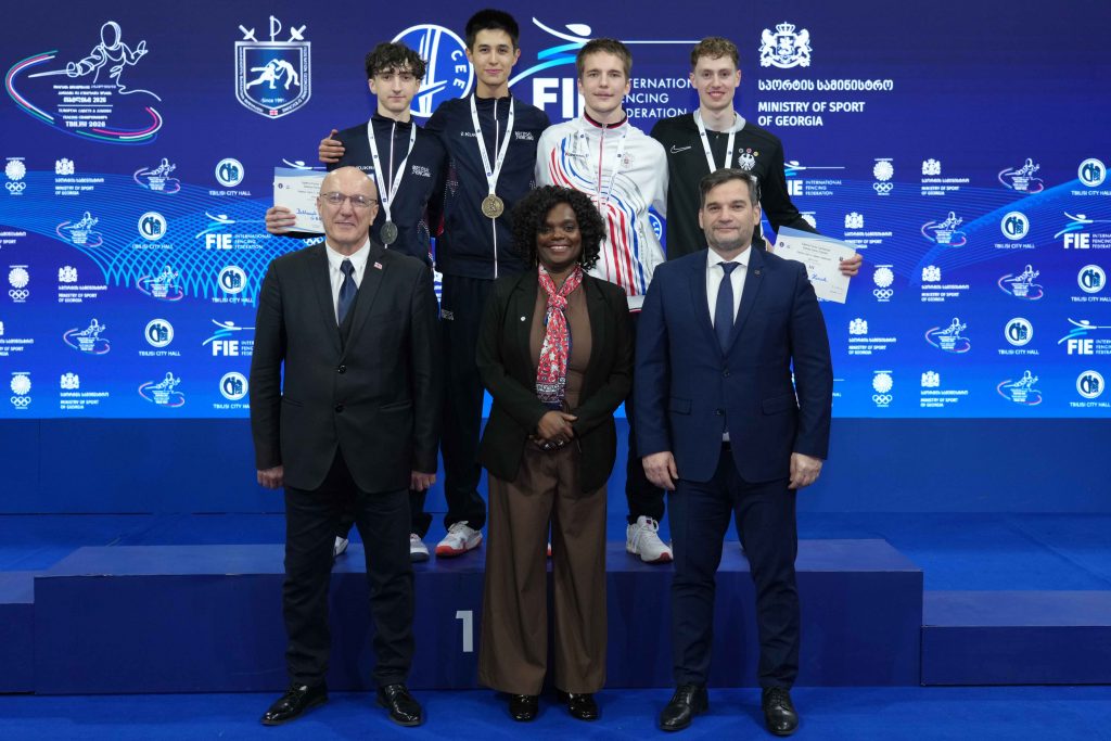 Four fencers on a podium wearing medals (L-R: GBR, GBR, RUS, GER). Three officials are in front of them.