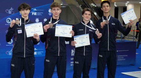 Four GBR fencers smile to the camera, holding up bronze medals and certificates