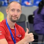 A coach smiles to the camera and gives a thumbs up.