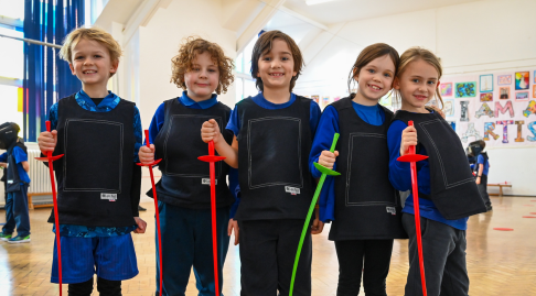 Five children smile to the camera, holding plastic swords.