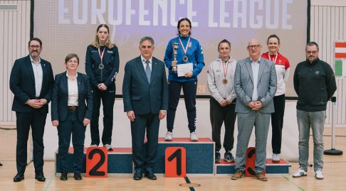 A podium photo with four fencers and several officials standing in front. L-R: GBR (Sophie Peat), ITA, SUI, AUT)