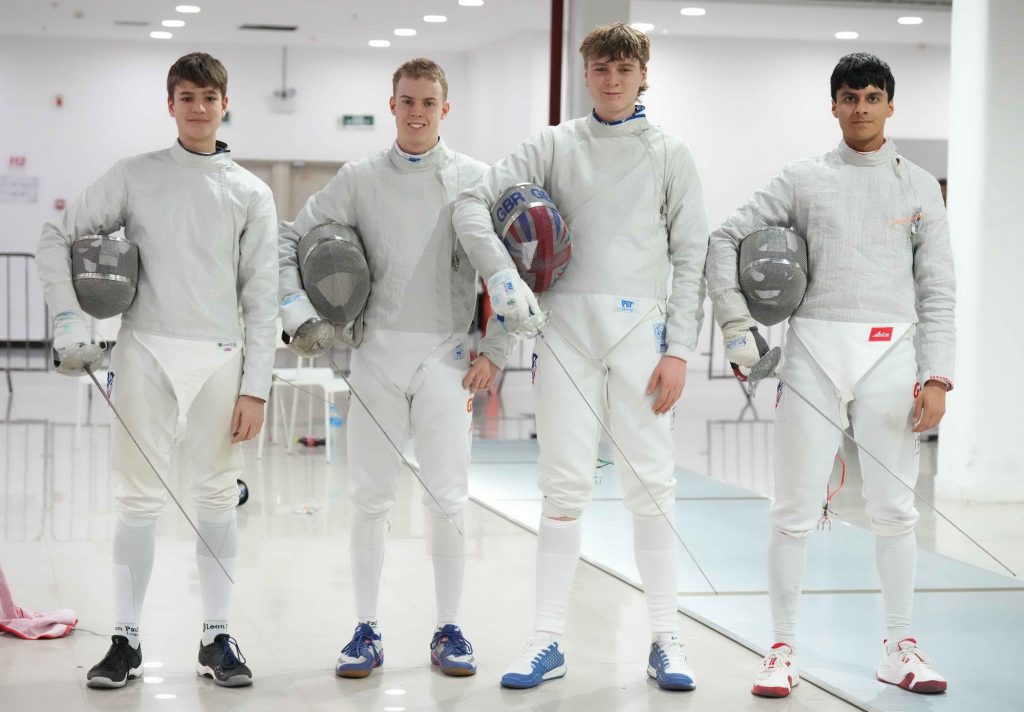 Four sabre fencers holding their mask and sword stand smiling to the camera.