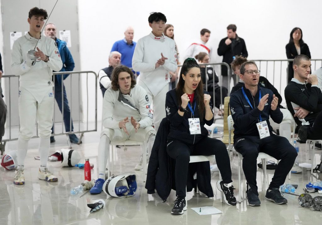Two coaches support the men's epee team at a competition.