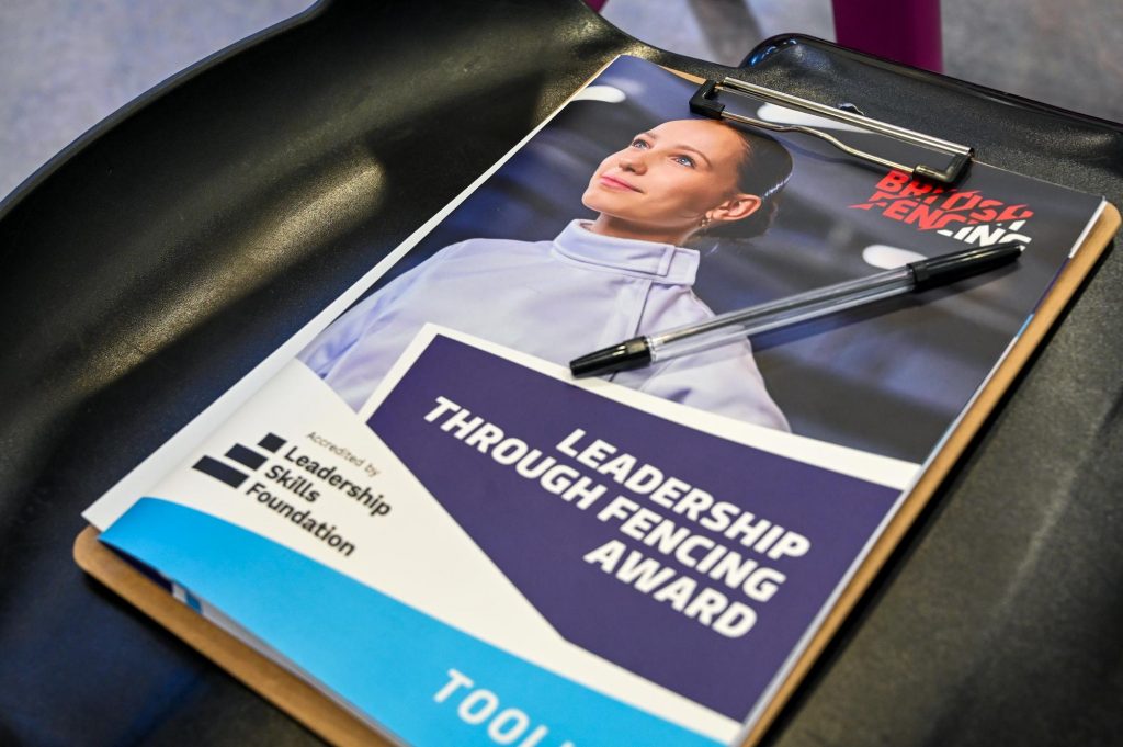 A Leadership Through Fencing toolkit workbook and pen are on a chair.