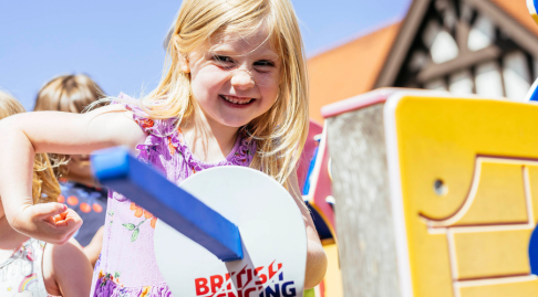 A child smiles while pointing a foam sword towards the camera