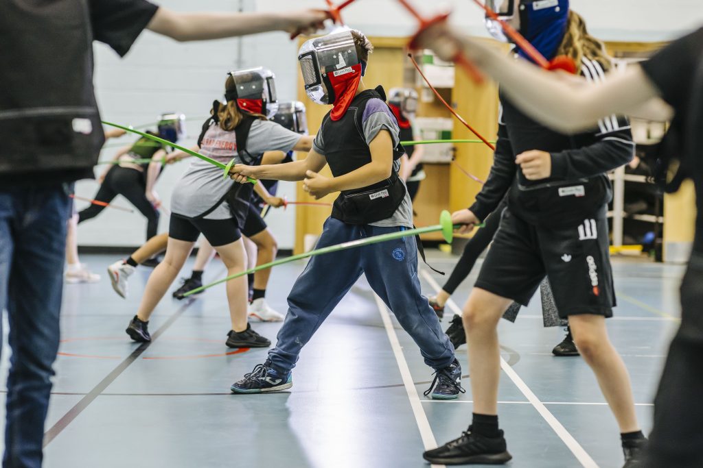 Several people are fencing using plastic kit in a sports hall