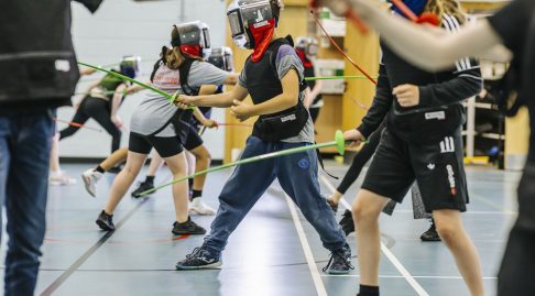 Several people are fencing using plastic kit in a sports hall