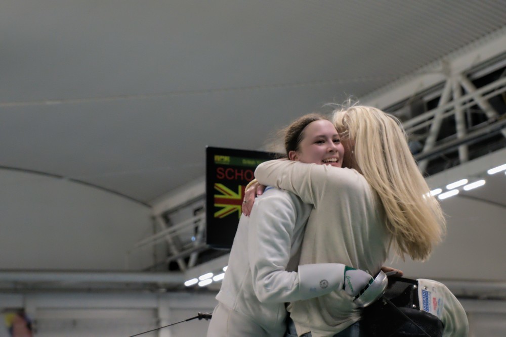 An epee fencer hugs their mother after winning.