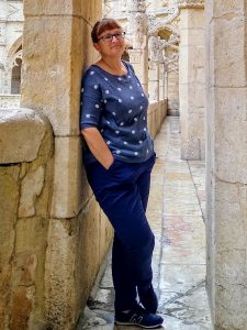 A woman stands leaning against a wall, smiling to the camera
