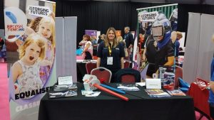A photo of Giulia Enright smiling to the camera behind a BF/We Are Forging Futures stand at the Summit.
