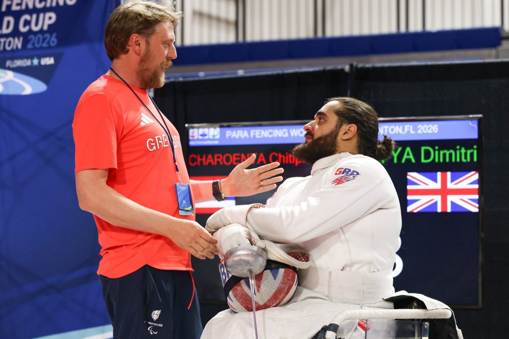 A fencing coach talks to a GBR epee para fencer during a match break