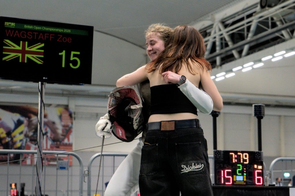 A foil fencer hugs their friend after winning a match