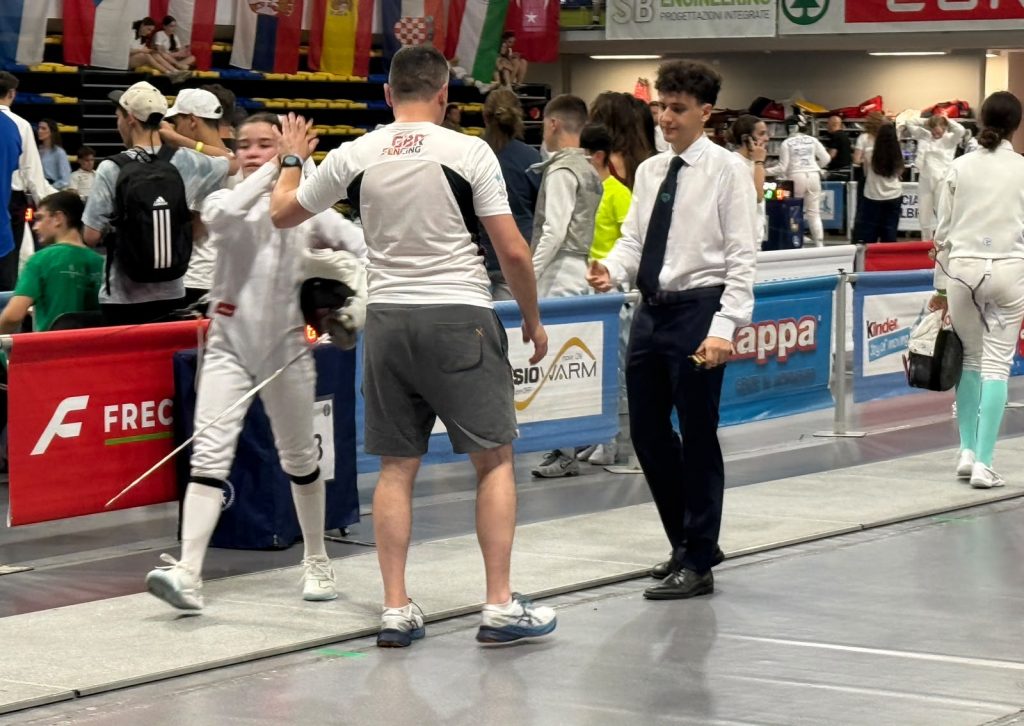 A foil fencer and GBR coach give a high five at a competition