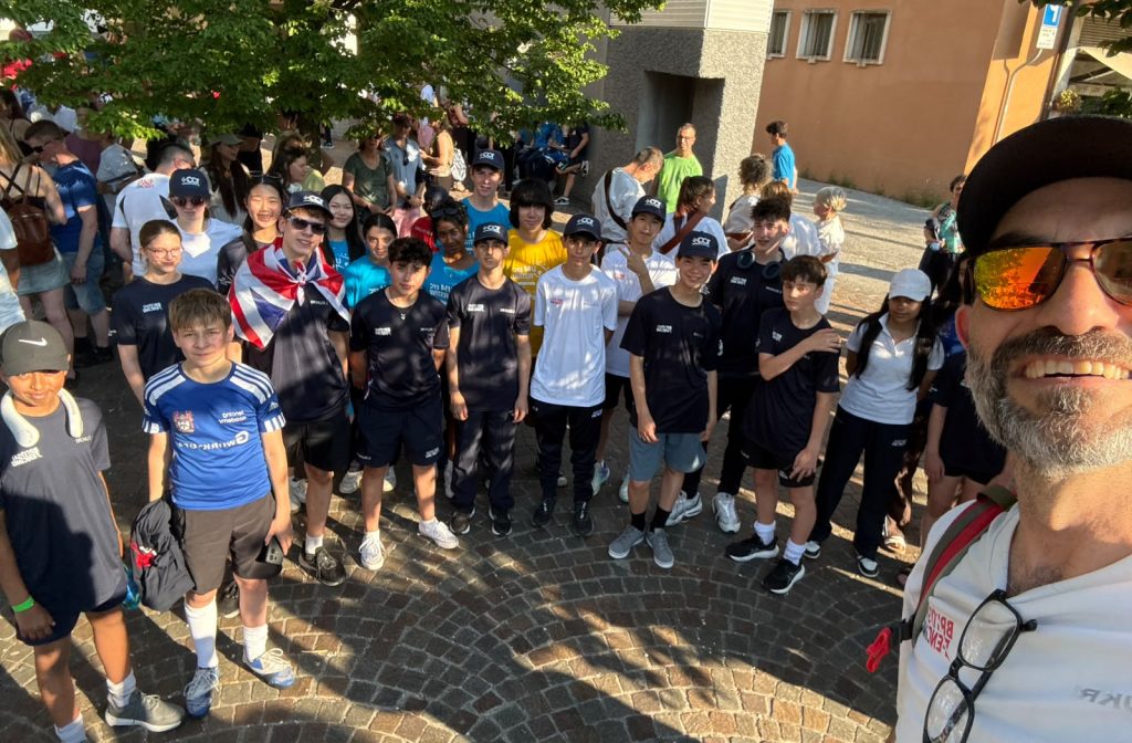 A large group of young fencers and Marco Zaffino smile for a selfie outside